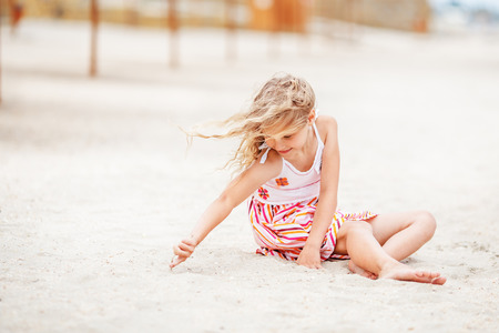 Portrait of a pretty little girl with waving in the wind long hair sitting on the beachの写真素材