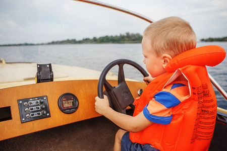 Little boy driving a motor boat on river firmly holding the steering wheelの写真素材