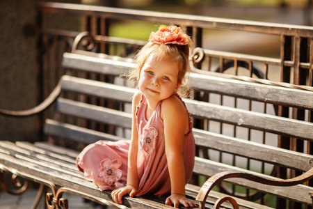 Portrait of a smiling pretty little girl sitting on a park benchの写真素材