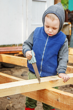 Little studious boy sawing a wooden board. Home construction. Little Helper. Little builder.の写真素材
