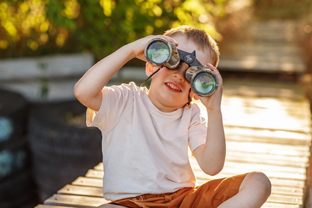 Little boy looking through binoculars sitting on the pier on river bankの写真素材