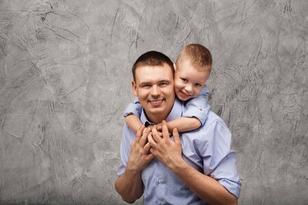 Father and little son in blue shirts in front of gray textured backgroundの写真素材