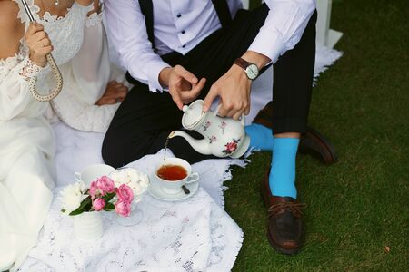 Bride and groom drink tea in bright clothes on the green grassの写真素材