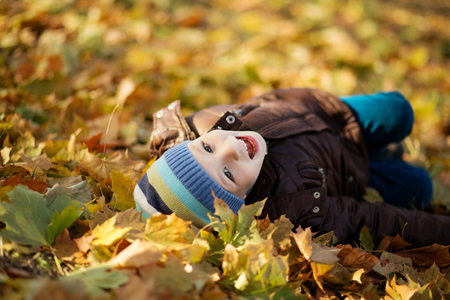 Portrait of a cheerful little boy wallow in fall foliage. Smiling funny little boy covered with autumn leaves. Little boy lying and having fun among multicolored autumn leaves in the parkの写真素材