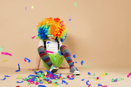 Happy clown boy with large colorful wig. Little boy in clown wig jumping and having fun. Portrait of a child throws up a multi-colored tinsel and confetti. Birthday boy.の写真素材