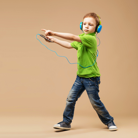 Dance! Handsome little stylish boy in headphones holding MP3 Player and dancing while standing against beige backgroundの写真素材