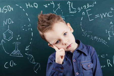 Genius boy near blackboard with formulas. Funny portrait clever pupil boy on school board background. Back to schoolの写真素材