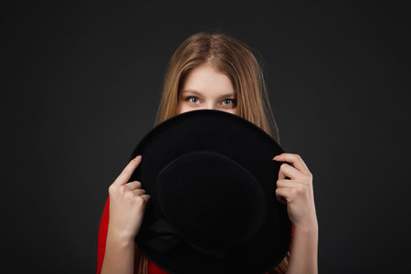 A beautiful girl dressed in red holding her hat. Girl holding hat up to faceの写真素材