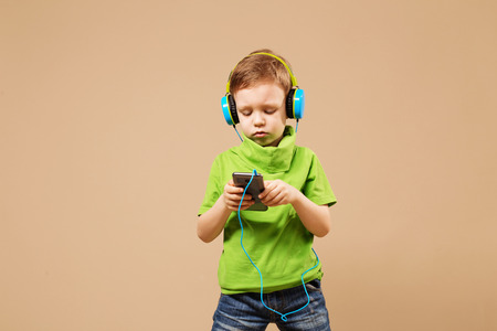 boy ware headphone and playing the cell phone on beige background. boy in the headphones enjoy music. young boy is listening to musicの写真素材