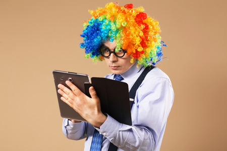 Businessman with tablet computer. Close-up Portrait of business man in clown wig using a tablet to access the internet. Business concept. Multitaskingの写真素材