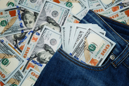 Macro shot of trendy jeans with american 100 dollars bills on its pocket. 100 dollar bill sticking out from a blue jean pocketの写真素材