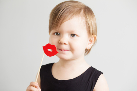 Portrait of a lovely little girl with funny red paper lips against a white backgroundの写真素材