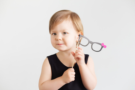 Portrait of a lovely little girl with funny photo props paper glasses against a white backgroundの写真素材