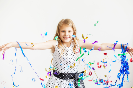 Little girl jumping and having fun celebrating birthday. Portrait of a child throws up multi-colored tinsel and confetti. Positive emotions. Happy excited laughing kid under sparkling confetti showerの写真素材
