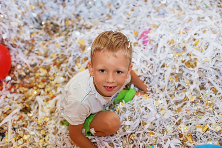 Little boy jumping and having fun celebrating birthday. Portrait of a child throws up multi-colored tinsel and paper confetti. Kids party. Happy excited laughing kid under sparkling confetti showerの写真素材