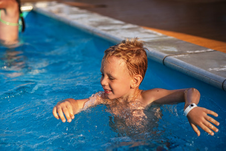 Happy kid playing in blue water of swimming pool. Little boy learning to swim. Summer vacations concept. Cute boy swimming in pool water. Child splashing and having fun in swimming poolの写真素材