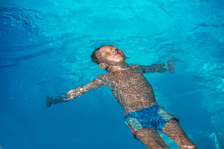 Happy kid playing in blue water of swimming pool. Little boy learning to swim. Summer vacations concept. Cute boy swimming in pool water. Child splashing and having fun in swimming poolの写真素材