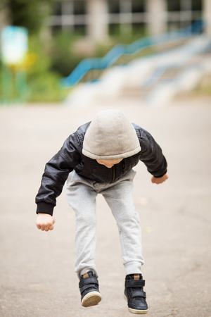 Full-length portrait of adorable little urban boy wearing black leather jacket. City style. Urban kids. Kid jumping and having fun outdoorsの写真素材