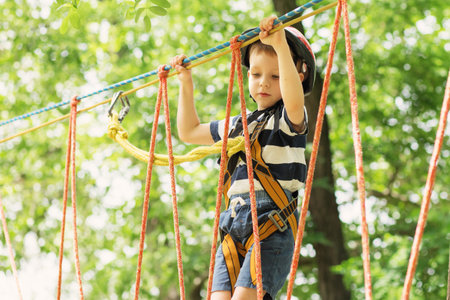 Kids climbing in adventure park. Boy enjoys climbing in the ropes course adventure. Child climbing...
