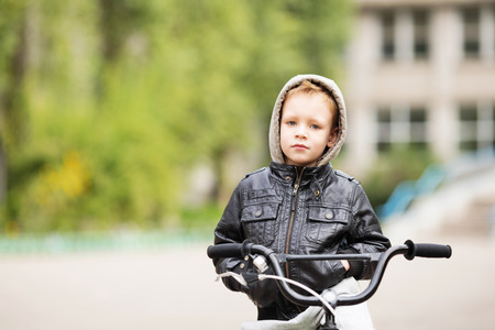 portrait of adorable little urban boy wearing black leather jacket. City style. Urban kids. The boy learns to ride a bike. Child driving a bicycle.の写真素材