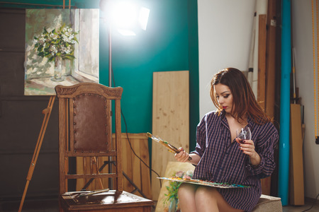 Woman artist painting a picture in loft studio. Creative pensive painter girl paints a colorful picture on canvas with oil colors in workshop. の写真素材