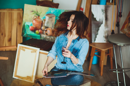 Woman artist painting a picture in loft studio. Creative pensive painter girl paints a colorful picture on canvas with oil colors in workshop.の写真素材
