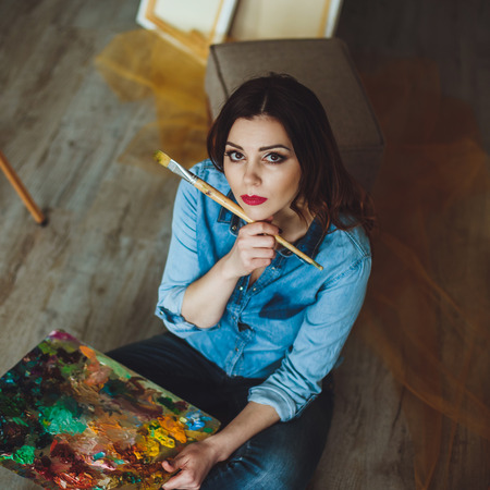 Woman artist painting a picture in a studio. Creative pensive painter girl paints a colorful picture on canvas with oil colors in workshop.の写真素材