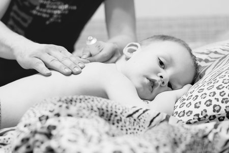 Father rubs the back of a sick child with ointment. Men's hands do massage to the child. Black and white photographyの写真素材