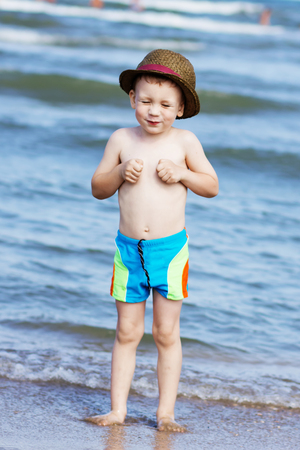 Funny little boy standing standing on the beach and laughing. The sea is cold for swimmingの写真素材