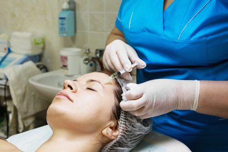 Beautician performs a needle mesotherapy treatment on a woman's faceの写真素材