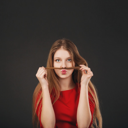 Cool young blonde Caucasian woman making mustache with her hair. Beautiful teenage girl making funny faces using her long blonde hair to make mustaches.の写真素材