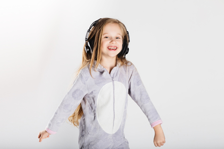 Cute little girl in headphones is using a smartphone, looking at camera and having fun at home. Day off, holiday, day of rest, free, off-timeの写真素材