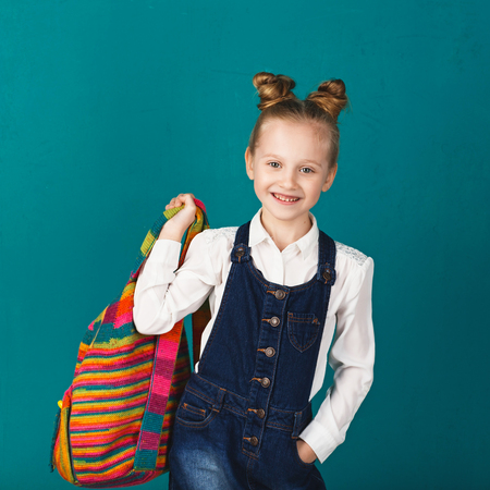 Funny smiling little girl with big backpack jumping and having fun against blue wall. Looking at camera. School concept. Back to Schoolの写真素材