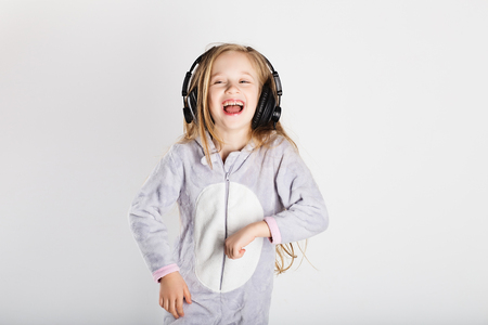 Cute little girl in headphones is using a smartphone, looking at camera and having fun at home. Day off, holiday, day of rest, free, off-timeの写真素材