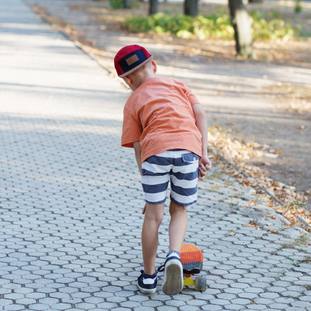 Little urban boy with a penny skateboard. Kid skating in a summer park. City style. Urban kids. Child learns to ride a penny boardの写真素材