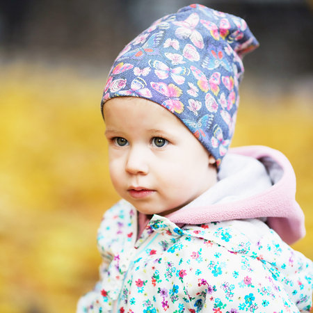 Happy urban little girl walking in city autumn park. Cute baby girl among the golden autumn maple leavesの写真素材