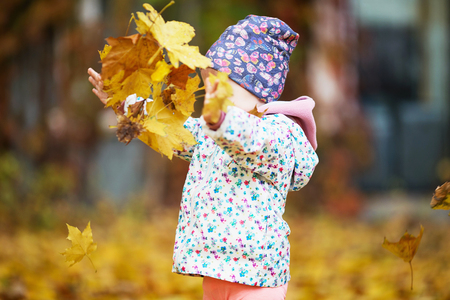 Happy urban little girl walking in city autumn park. Cute baby girl among the golden autumn maple leavesの写真素材