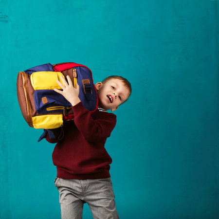 Funny little boy with big backpack jumping and having fun against turquoise wall. School concept....