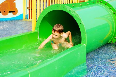 Funny child playing in water park splashing water. Summer holidays concept. Boy has into pool after going down water slide during summer. Kid on water slide at aquapark. の写真素材