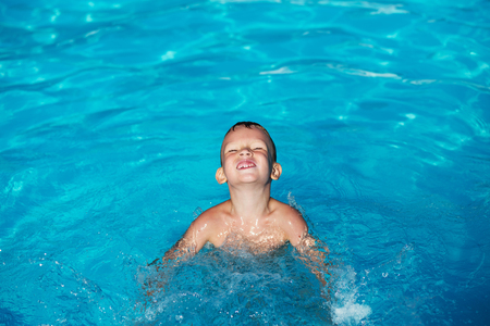Happy kid playing in blue water of swimming pool. Little boy learning to swim. Summer vacations concept. Cute boy swimming in pool water. Child splashing and having fun in swimming poolの写真素材