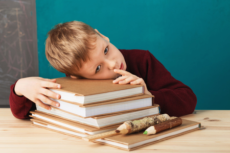 tired school boy asleep on books. little student sleeping on textbooks. Child in school uniform lies on the table with big pile of books against blue wall. School concept. Back to schoolの写真素材