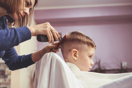 Little boy at the hairdresser. Child is scared of haircuts. Hairdresser's hands making hairstyle to little boy, close upの写真素材