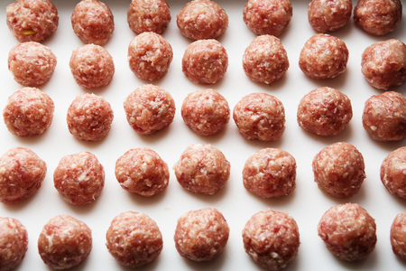 Freshly cooked raw meatballs lie on a white plastic kitchen board.の写真素材