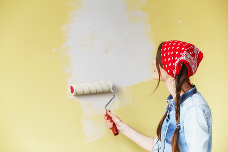 Beautiful girl in red Headband painting the wall with paint roller. Portrait of a young beautiful woman painting wall in her new apartmentの写真素材