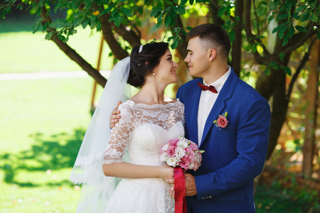 Just married loving hipster couple in wedding dress and suit in the park. Happy bride and groom walking in the beautiful garden. Romantic Married young family. Summer weddingの写真素材