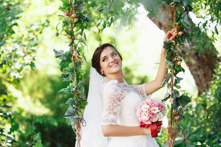 Beautiful brunette bride with bouquet outdoor. Happy bride outdoors. Beautiful bride posing in her wedding dayの写真素材