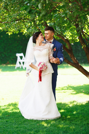 Just married loving hipster couple in wedding dress and suit in the park. Happy bride and groom walking in the beautiful garden. Romantic Married young family. Summer weddingの写真素材