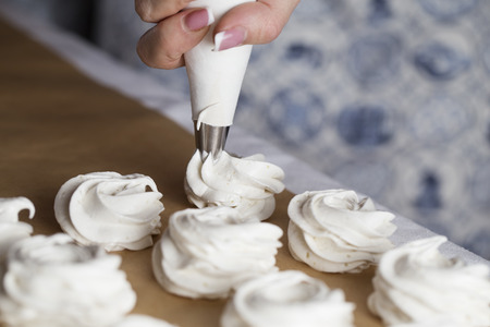 The process of making marshmallow. Close up hands of the chef with confectionery bag cream to parchment paper at pastry shop kitchenの写真素材
