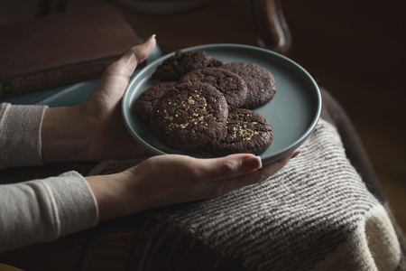 Chocolate cookies on the plate. Female hands holding a plate of chocolate chip cookies.の写真素材