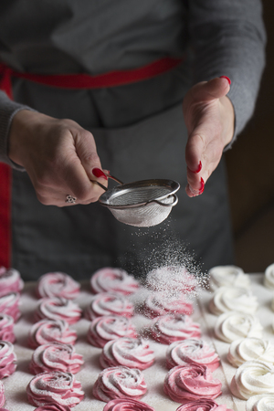 The process of making marshmallow. Close up hands of the chef with metal sieve sprinkling zephyr with powdered sugar at pastry shop kitchen.の写真素材